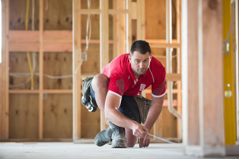 New Zealand Certified Builders ; A man measuring inside a home being built with only wooden studs installed.