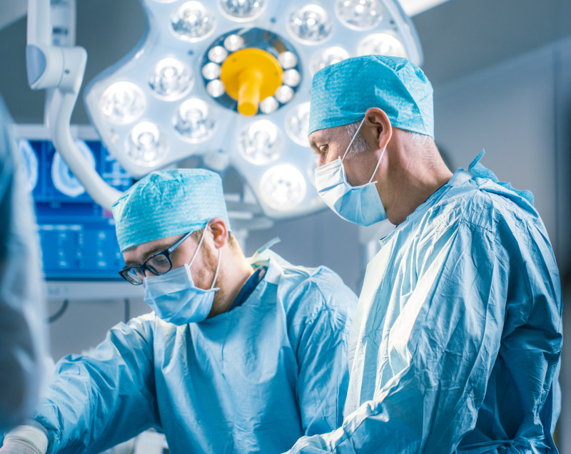 Australian Society of Plastic Surgeons (ASPS) - Sydney, New South Wales Shot In Operating Room of Two Surgeons During the Surgery Procedure Bending Over Patient with Instruments. Professional Doctors in Modern Hospital